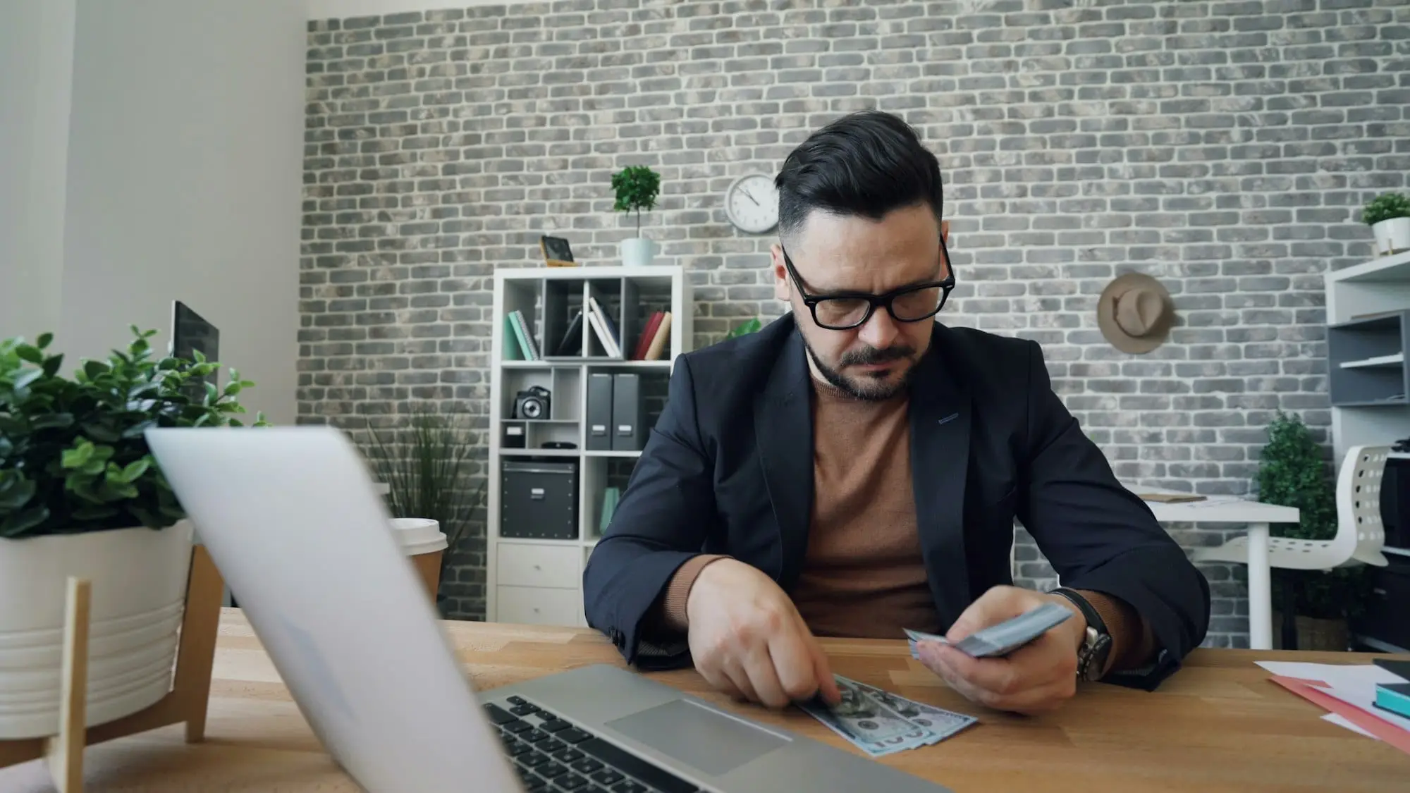 An accountant at a desk counting banknotes beside an open laptop